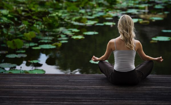 A woman meditating by a lotus pond – a peaceful setting to connect with emotional, spiritual and physical energy.